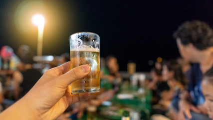 Hand holding beer mugs and backgrounds with candlelight and people
