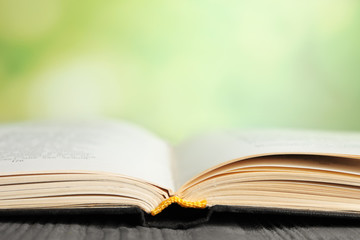 Open book on blue wooden table against blurred green background, closeup. Space for text