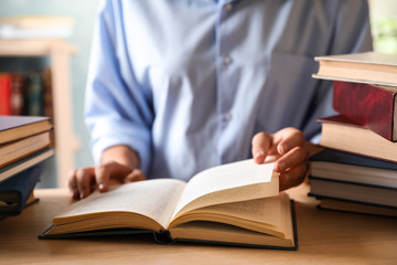 Woman reading hardcover book at wooden table indoors, closeup