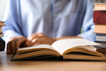 Woman reading hardcover book at wooden table indoors, closeup