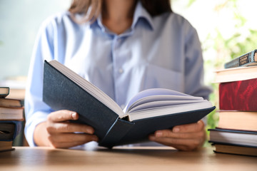 Woman reading hardcover book at wooden table indoors, closeup