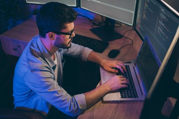 Profile photo of it specialist guy working late at night sitting comfy office chair holding hands on keyboard looking monitors website debugging expert dark office indoors
