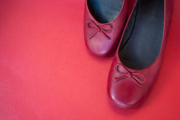 Stylish female flat shoes in dark red color on dark red background with copyspace. Beauty and fashion concept.