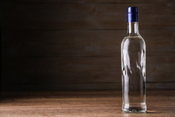Bottle of vodka on table against wooden background. Space for text