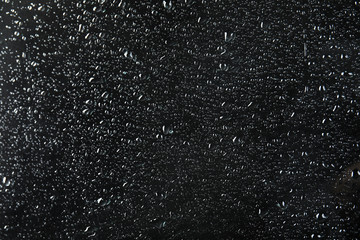 Glass with rain drops against dark background