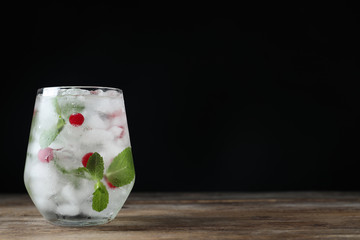 Vodka cocktail with cranberries and ice on wooden table against black background. Space for text