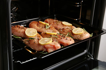Chicken breasts with lemon and rosemary on baking sheet in oven