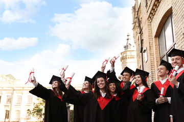 Happy students with diplomas outdoors. Graduation ceremony