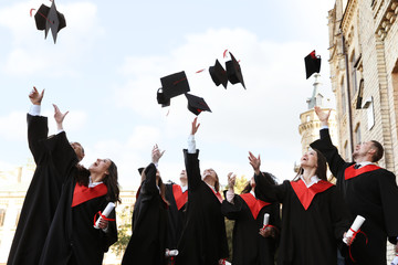 Happy students with diplomas throwing graduation hats in air outdoors