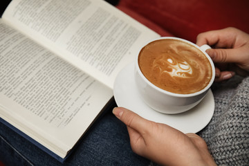 Woman with cup of coffee reading book, closeup