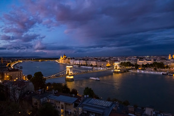 Night aerial panorama of Budapest with Chain Bridge and Parliament buliding and river boats on Danube river illuminated with night lights.
