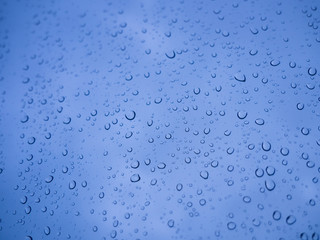 Rain drops on car window glasses surface, water drops with natural blue background.