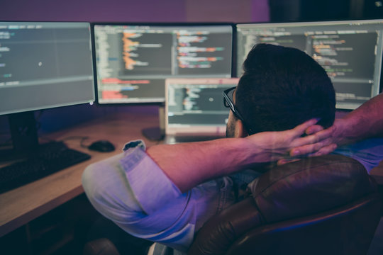 Rear view photo of it specialist guy sitting comfy office chair holding hands behind head looking many monitors testing ip address waiting team finishing debugging