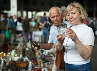 Attentive mature spouses buying retro handicrafts on flea market