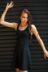 Fototapeta premium Brunette young woman in sexy Black dress, studio wall indoor