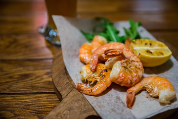 fried roasted shrimps with lemon and arugula on wooden table