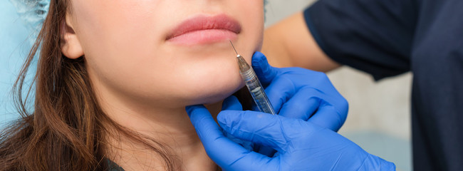 Cosmetologist makes lip augmentation procedure in a beauty salon. The beautician injects hyaluronic...