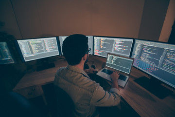 Rear back behind view of his he nice senior experienced skilled smart clever brunet guy monitoring many screens tech hardware optimization solution in dark beige room workplace station indoors