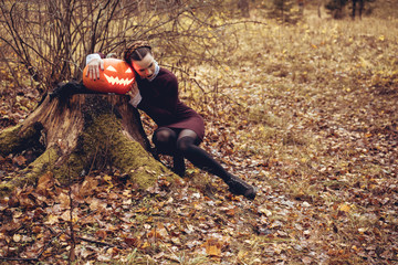 Halloween Witch with a carved Pumpkin in a autumn forest. Beautiful young woman in witches dress...