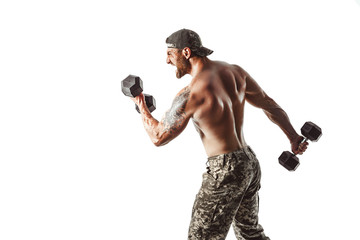 Muscular athlete bodybuilder man in camouflage pants with a naked torso punching with dumbbells...