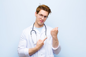 young red head doctor looking impatient and angry, pointing at watch, asking for punctuality, wants...