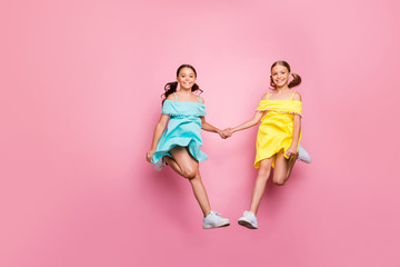 Full body photo of two small sisters girlfriends jumping high walking home together last studying day wear blue yellow dresses isolated pink color background