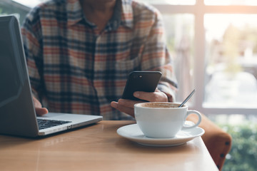 Man using smart phone in cafe and working on laptop computer