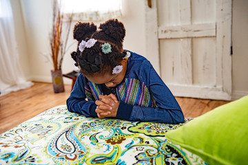 African American girl prays by the side of her bed..