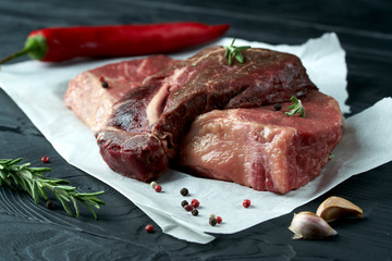 Raw fresh meat on paper with herbs, pepper and garlic on dark background