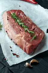 Raw fresh meat on paper with herbs, pepper and garlic on dark background