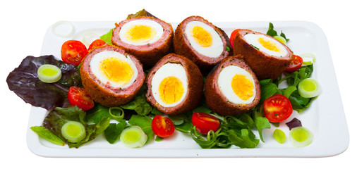 Tasty scotch eggs served with greens, leek and tomatoes at plate