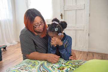 African mother and daughter pray together at side of bed.