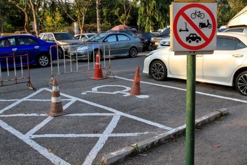 Prohibition signs to do not park various types of vehicles on sign board pole, white marking lines and handicapped parking spot on asphalt floor next to car park and roadside.