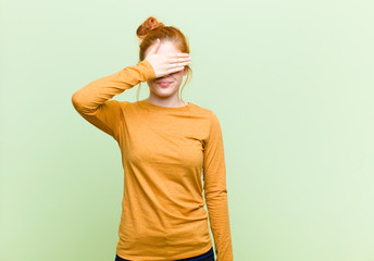 young pretty red head woman covering eyes with one hand feeling scared or anxious, wondering or...