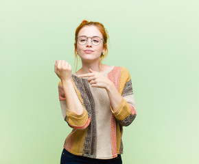 young pretty red head woman looking impatient and angry, pointing at watch, asking for punctuality,...