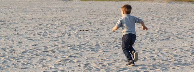 Little kid boy running on sand at the beach