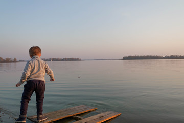 Fototapeta premium Little boy child throws plants into the water