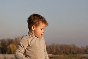 Little kid boy dreaming, pensive, on the beach near the water