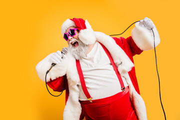 Merry x-mas carols from crazy overweight white hair christmas grandfather hold microphone sing song on noel time celebration wear style trendy suspenders hat headwear isolated yellow color background - Powered by Adobe