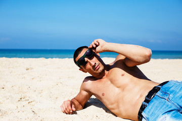 young muscular man resting and posing on the beach. 