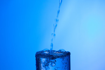 vaso lleno de agua en el que cae un chorro de agua externo produciendo un chapoteo y gotas que...