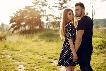 Fototapeta premium Cute couple in a park. Lady in a black dress. Guy in a black t-shirt.