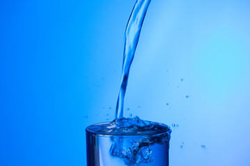 Agua entrando en un recipiente transparente de crital o plástico; agua salpicando 