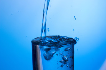 Agua cayendo en un vaso lleno produciendo chapoteo y que el agua sobresalga y caiga fuera mojñandolo todo