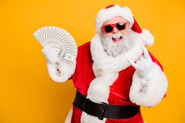 X-mas lottery win credit bank present for noel. Funky crazy hipster white bearded santa claus hold money fan show horned symbol enjoy deposit gift wear red hat isolated yellow color background