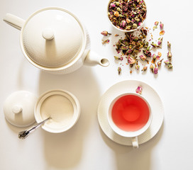 Herbal tea of roses in two white cups, teapot, sugar bowl on a white background, top view.