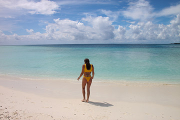 back girl with a yellow bikini walking towards the beach