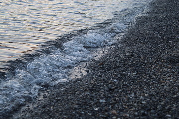 Shore of the beach with a wave breaking and where the crystal clear water, sand and stones appear