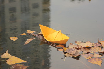 Yellow homemade origami paper boat on the river water in the autumn park