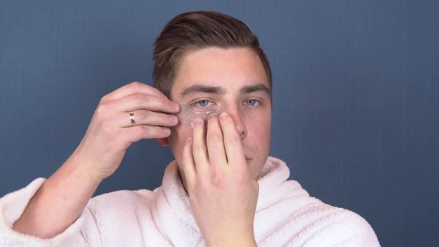 A young man puts patches on his face. Blue hydrogel patches for rejuvenating the skin of the face. Man sitting in a white coat. Close up